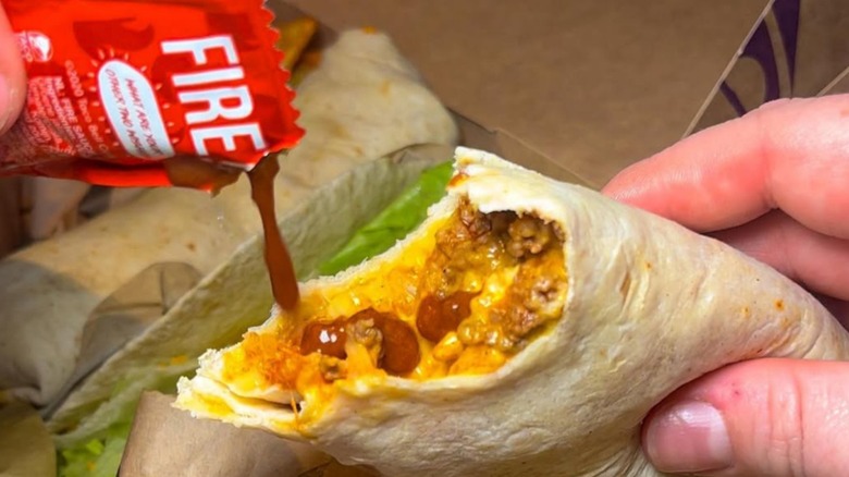 Hand squeezing a packet of Fire sauce onto a burrito