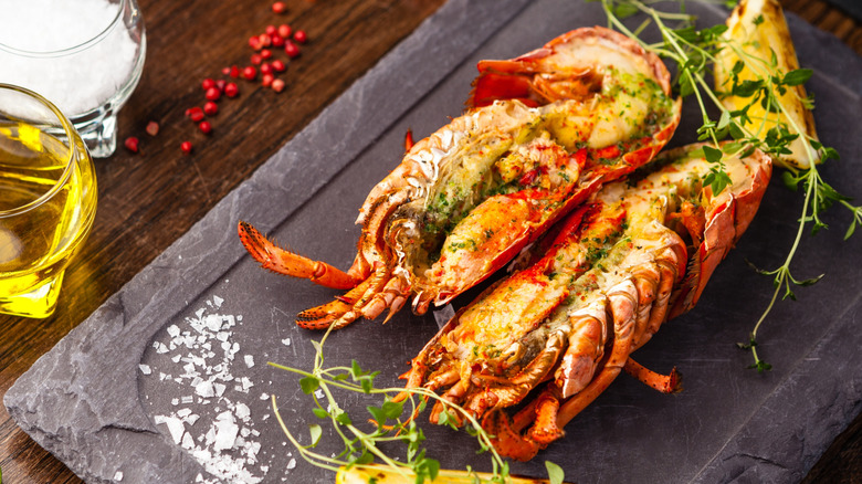 Sliced, cooked lobster on a slate board with lemon and herbs