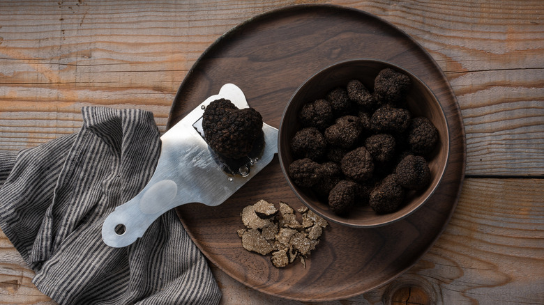 A bowl of black truffles on a table, with a slicer and several sliced pieces