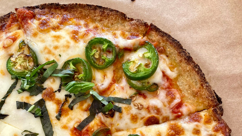 Section of cheese pizza with jalapeños and basil