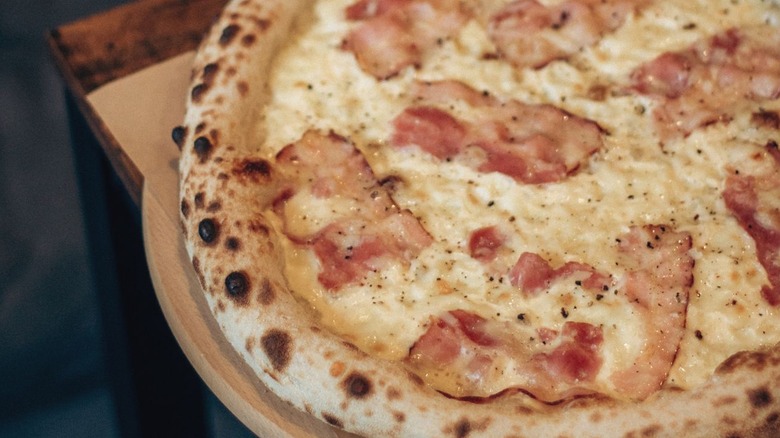 Section of white cheese pizza with bacon topping