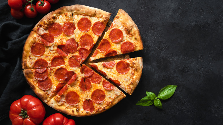 Pepperoni pizza with slices cut on black background