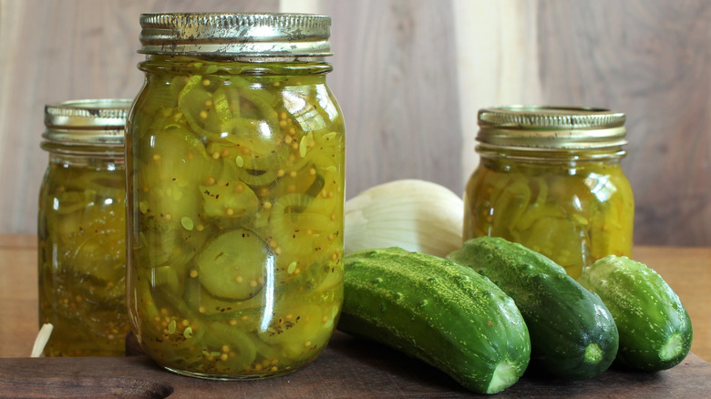 Jarred sweet pickles next to cucumbers