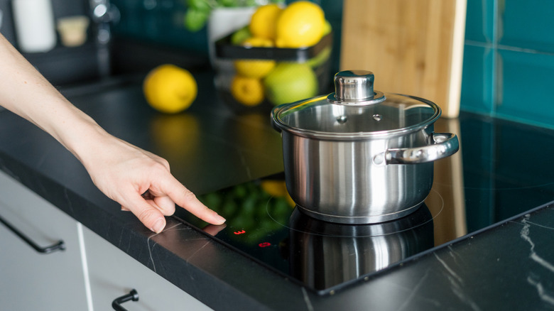 A person pressing a button on an induction stove with a pot on it