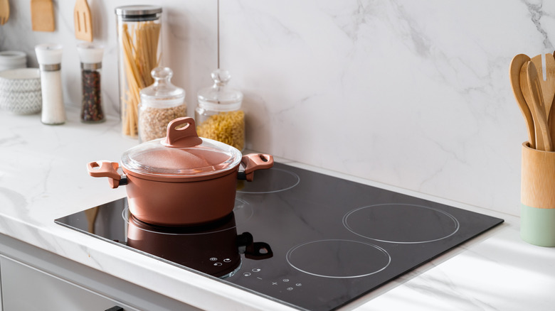 A pot on an induction stove next to pasta in glass jars
