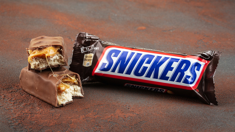 Snickers candy bar in wrapper with bar cut in half next to it.