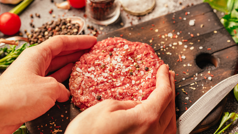 Hands seasoning a raw beef patty