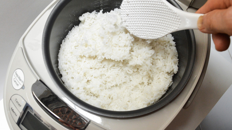 Someone scooping rice out of an automatic rice cooker