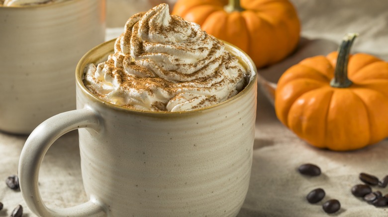 A pumpkin spice latte in a mug next to small pumpkins
