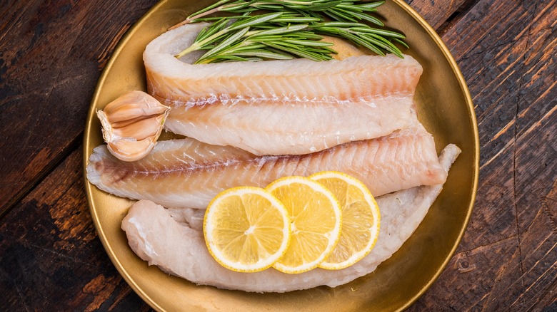 Raw pollock fillets with rosemary, lemon slices and garlic.