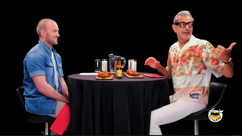 Sean Evans and Jeff Goldbum sit across from one another, with Goldblum gesturing to someone off camera