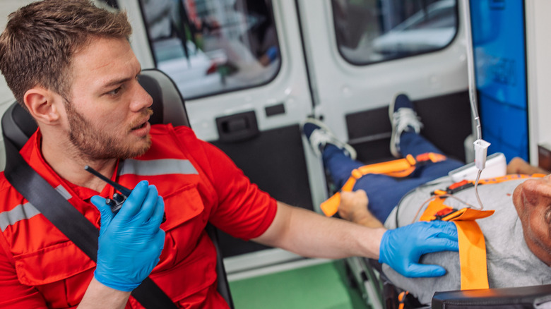 a paramedic wearing blue safety gloves talks to a patient on a stretcher