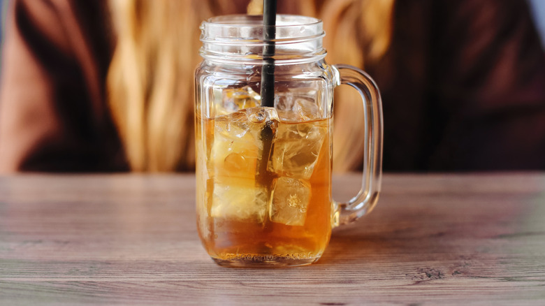 a glass mason jar full of iced tea on a table