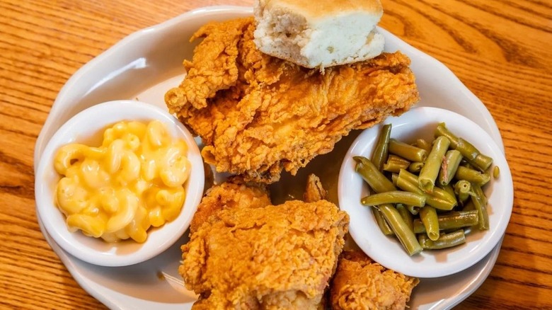 a plate with three pieces of fried chicken, mac and cheese, green beans, and a biscuit