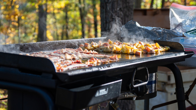 Bacon and potatoes cooking on an outdoor griddle
