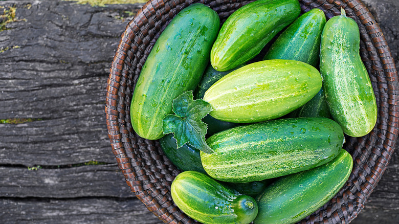 Top down shot of a selection of fresh cucumbers in a basket o a wooden table