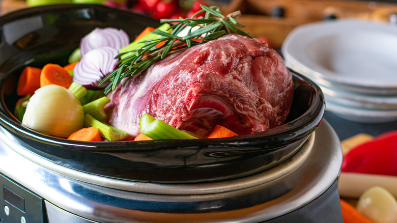uncooked pork roast with root vegetables in a slow cooker
