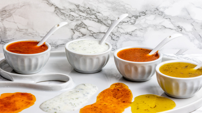 Four different dressings in white bowls on marble background