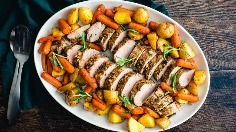 White platter of roast pork tenderloin medallions surrounded by vegetables