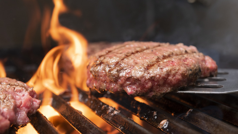 A burger on a flaming grill with a spatula lifting it up