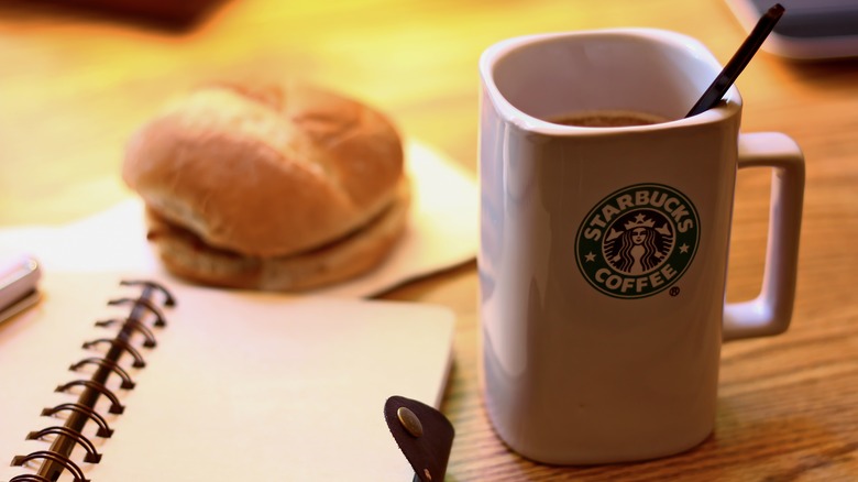 A Starbucks cup of coffee next to a notebook and a breakfast sandwich behind 