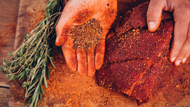 Hands applying a dry rub to meat