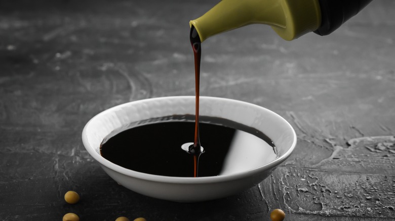 Soy sauce being poured into a white glass bowl