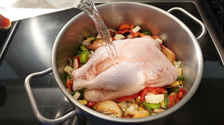 Whole chicken in pot with aromatics and water pouring