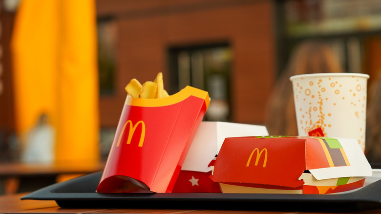 A tray of packaged McDonald's food, like french fries, a box for a burger, and a paper cup, alone at a table