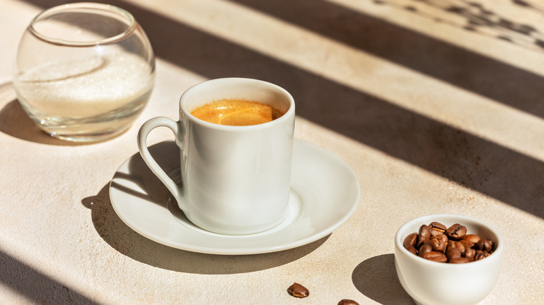 a mug of coffee sits between a bowl of water and cup of beans