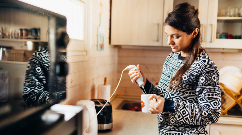 A woman uses a milk frother in mug