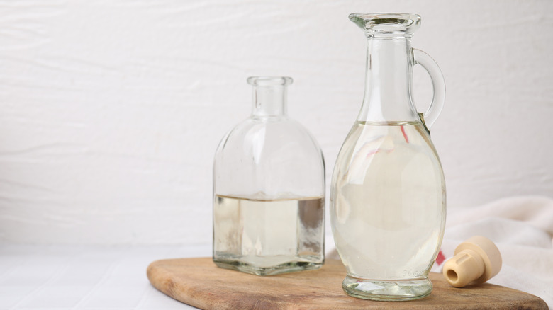 Two different-shaped bottles of vinegar on a wooden board with a cork and white background