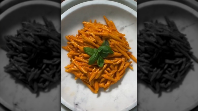 Penne in orange sauce basil leaves in white marble