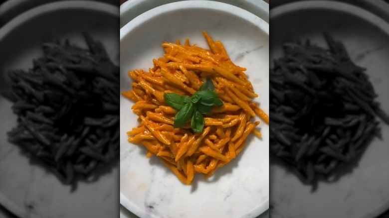 Penne in orange sauce basil leaves in white marble