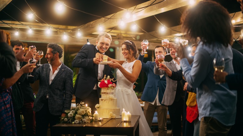 bride and groom holding slice of wedding cake with people