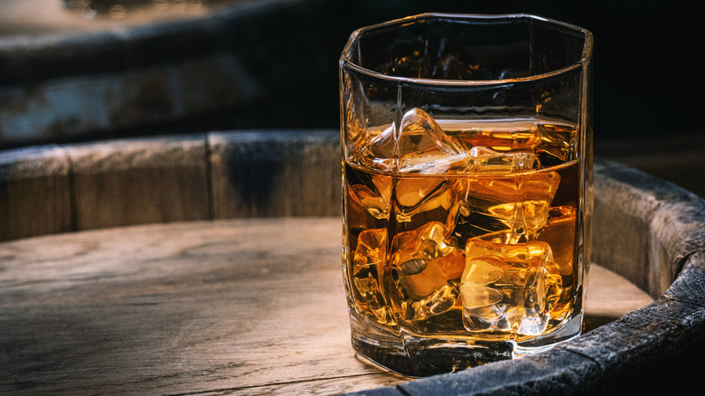 glass of bourbon with ice sits on barrel