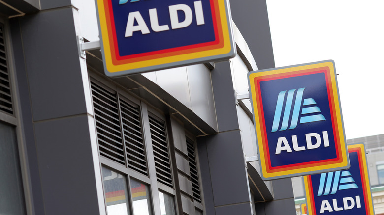 Three square Aldi signs in a row, mounted on a gray wall