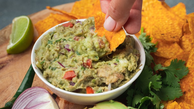 person dipping chip into chunky guacamole