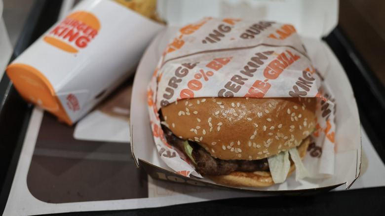 A Burger King Whopper in its packaging, on a serving tray