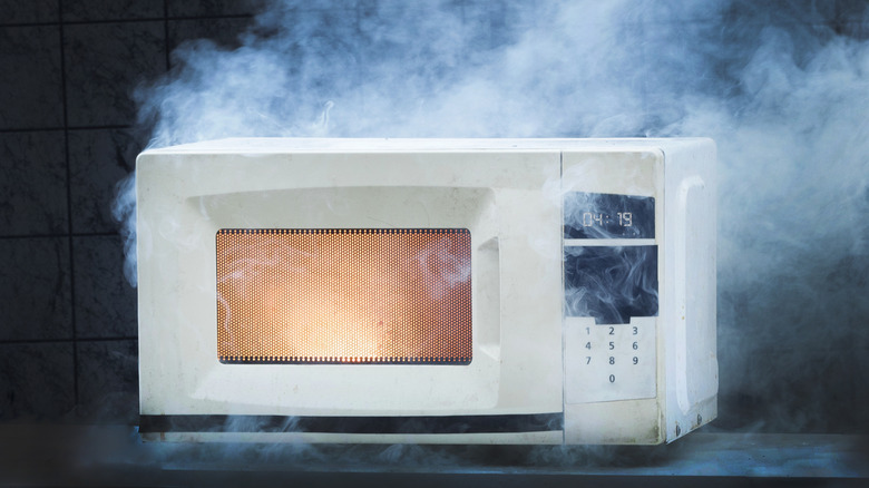 White microwave with fire inside and smoke coming out because of improper operation