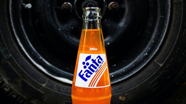 Bottle of orange Fanta in front of the wheel of a vehicle