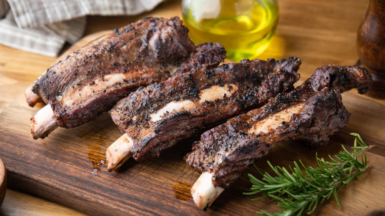 Four cooked beef back ribs on wooden cutting board.