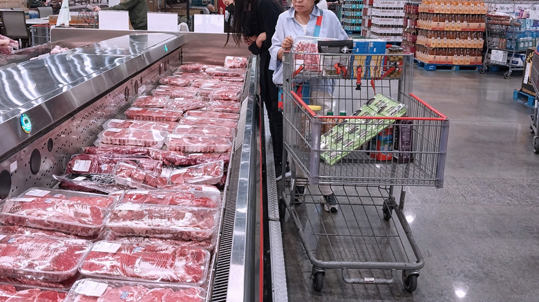 Costco shopper pushing cart through meat aisle.
