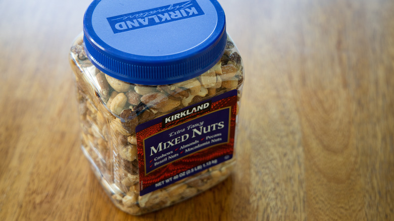 A container of Kirkland extra fancy mixed nuts with a blue lid on the plastic container atop a wooden table.