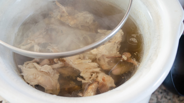 Close up of chicken in water in a Crock-Pot with the lid partially open above