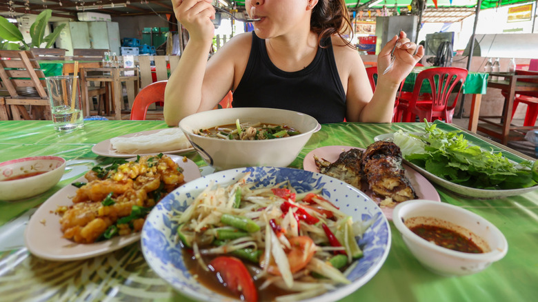 Woman dines solo and eats several dishes at an outdoor Thai restaurant
