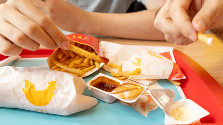 Two people dipping McDonald's fries in sauce containers