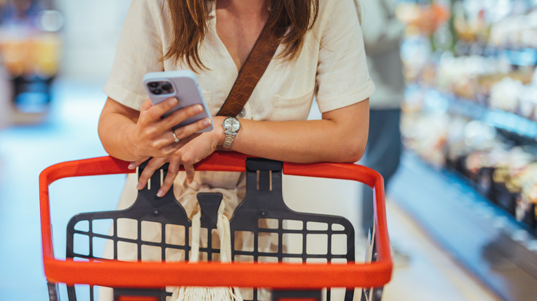 shopper using phone at grocery store over shopping cart