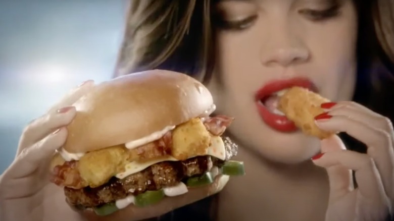 A still from a Hardee's commercial, in which a woman holds a Hardee's burger while biting a chicken nugget
