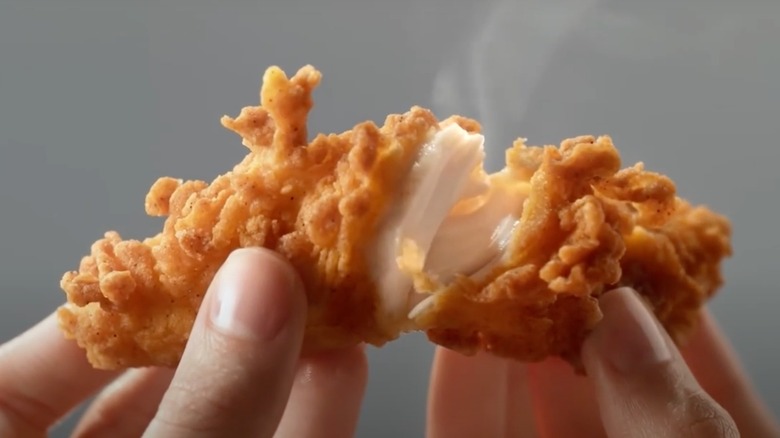 A pair of hands break apart a chicken tender